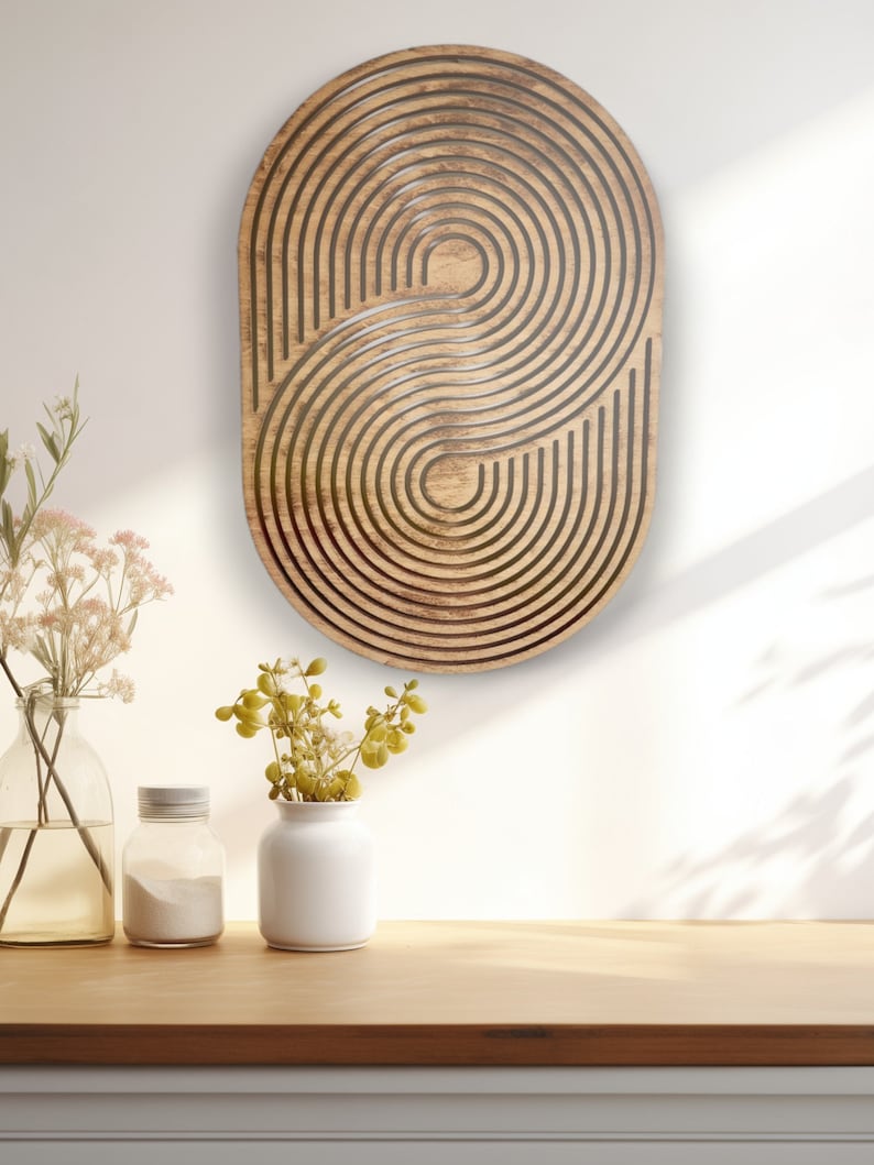 May include: A wooden wall decor with a geometric pattern of concentric circles and ovals in a light brown color. The decor is hanging on a white wall above a wooden countertop with two vases and flowers.
