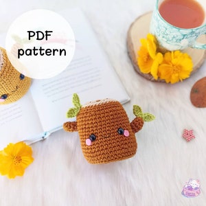 Pode incluir: Um padrão de crochê para um tronco de árvore marrom bonito com um rosto feliz e folhas verdes. O padrão está disponível para download em PDF.