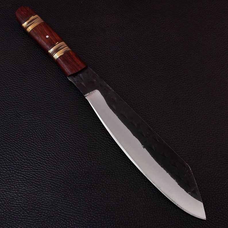 May include: A long, sharp, silver knife with a dark brown wooden handle and gold accents. The knife is lying on a black textured surface.