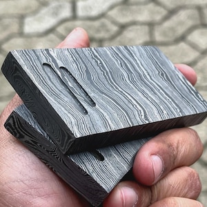 May include: Two stacked rectangular pieces of metal with a patterned surface. The top piece has two long, narrow grooves cut into it.
