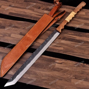 Può includere: Una lama lunga, affilata, d'argento con un manico in legno e un fodero in pelle marrone. La lama ha una leggera curva ed è molto affilata. Il manico è in legno e presenta un design decorativo. Il fodero è in pelle marrone e ha una cinghia per il trasporto.