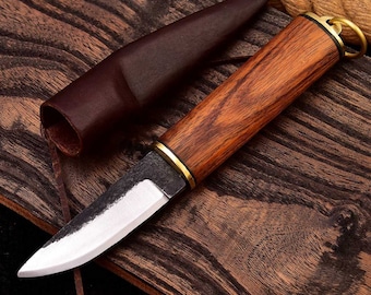 May include: A small, brown-handled knife with a brass ring on the handle. The blade is made of steel and has a slight curve. The knife is sitting on a wooden surface with a leather sheath.