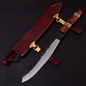 May include: A black and silver knife with a wooden handle and a leather sheath. The knife has a textured blade and a brass accent on the handle.