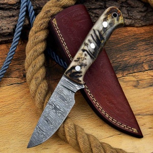 May include: A  knife with a  damascus steel blade and a  brown and white patterned handle. The knife is in a brown leather sheath.