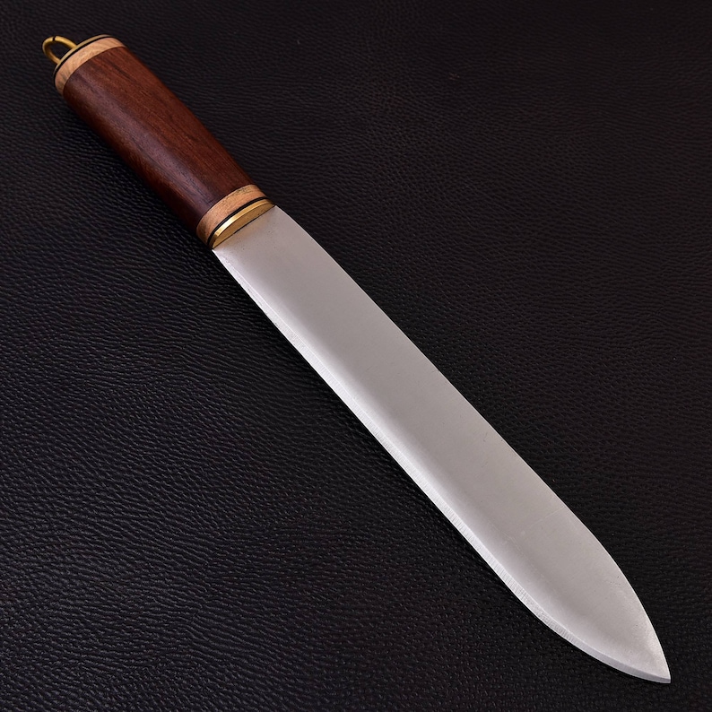 May include: A handcrafted knife with a dark wood handle and a polished steel blade. The handle is accented with brass rings and a small loop at the end. The blade is approximately 12 inches long, with a sharp edge and a pointed tip.