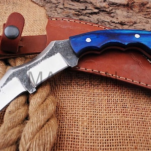 May include: A curved, silver knife with a blue and black wooden handle. The knife has a leather sheath with stitching around the edges.