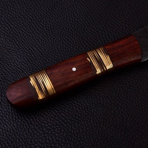 May include: A wooden knife handle with gold accents and a white dot. The handle is made of dark wood and has a smooth finish.