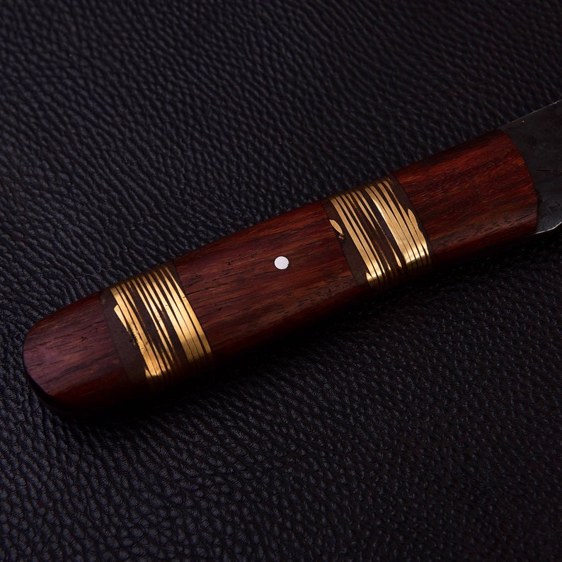 May include: A wooden knife handle with gold accents and a white dot. The handle is made of dark wood and has a smooth finish.
