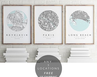 May include: Three framed city maps with a light blue background and black lines. The maps are of Reykjavik, Iceland; Paris, France; and Long Beach, California. The text "ANY 3 LOCATIONS FREE US SHIPPING" is in a circle below the maps.