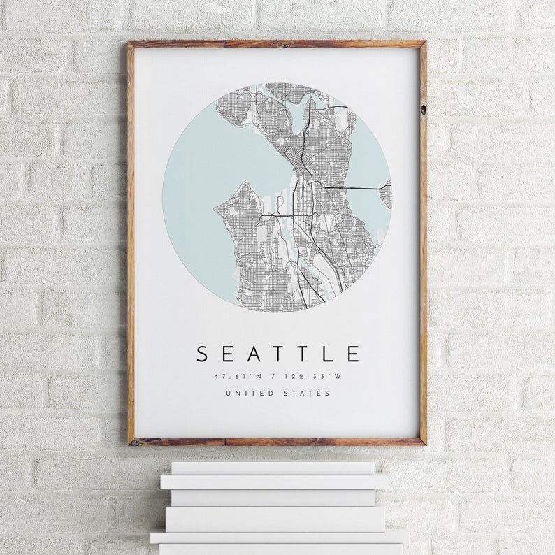 K&ouml;nnte beinhalten: Ein gerahmter Druck einer Karte von Seattle, Washington, mit hellblauem Hintergrund und schwarzen Linien. Der Text "Seattle" ist unter der Karte gedruckt, zusammen mit den Koordinaten "47.61'N / 122.33'W" und "Vereinigte Staaten".