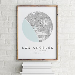 K&ouml;nnte beinhalten: Ein gerahmter Druck einer Karte von Los Angeles, Kalifornien, in einem Kreis mit hellblauem Hintergrund. Der Text unter der Karte lautet "Los Angeles, 34.05&deg;N / 118.24&deg;W, Vereinigte Staaten."
