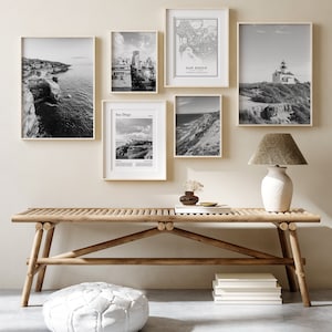 Puede incluir: Un banco de madera con un puf blanco delante. Hay fotos enmarcadas en blanco y negro en la pared detrás del banco. Las fotos son de un faro, un horizonte de la ciudad, una playa y un mapa de San Diego.