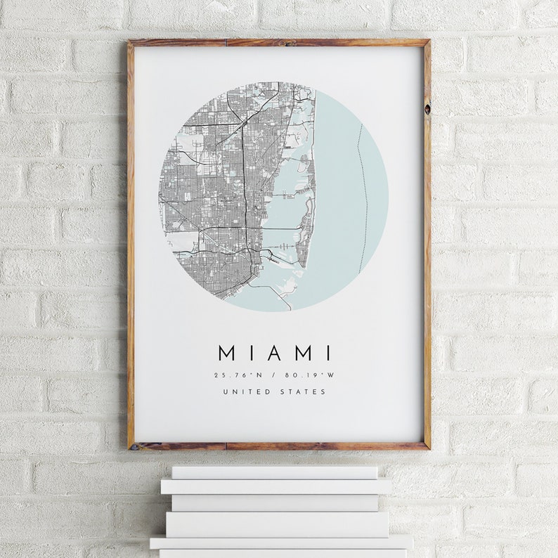 May include: A framed print of a map of Miami, Florida. The map is in a circle with a light blue background. The text "MIAMI" is below the map, along with the coordinates "25.76&deg;N / 80.19&deg;W" and "UNITED STATES".