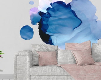 May include: A modern living room scene featuring a light gray sofa with several pillows and a pink throw blanket. The wall behind the sofa has a large abstract art piece in shades of blue. A gold lamp is in the background.