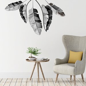 May include: A modern interior scene featuring a gray armchair with a yellow pillow, a small wooden side table with a bonsai tree, and large black and white leaf wall art. The room has a minimalist design with light wood flooring.