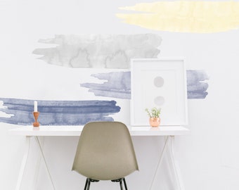 May include: A white desk with a white chair, a framed picture, a small potted plant, and a candle. The wall behind the desk has four watercolor brushstroke decals in shades of gray, blue, and yellow.