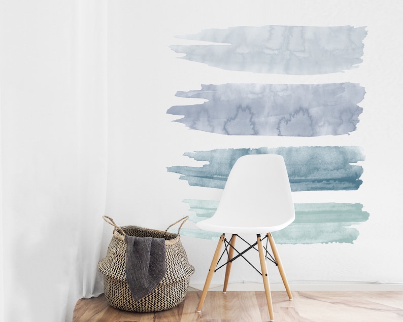 May include: Four horizontal watercolor brushstrokes in shades of blue and green on a white wall. The brushstrokes are arranged in a graduated pattern, with the darkest blue at the top and the lightest green at the bottom. A white chair with wooden legs sits in front of the wall.