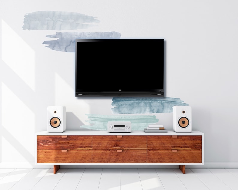 May include: A wooden entertainment center with four drawers and a white top. A flat screen TV is mounted on the wall above the entertainment center. Two white speakers with gold accents are on either side of the entertainment center. The wall behind the entertainment center has a light blue and green watercolor design.