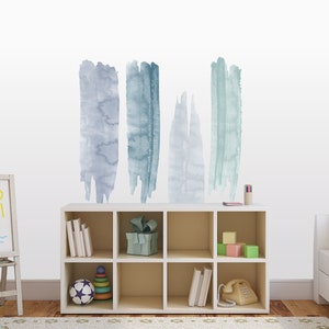 May include: A white bookshelf with six shelves, filled with books, toys, and a phone. The wall behind the bookshelf has five blue and gray watercolor brushstroke decals.