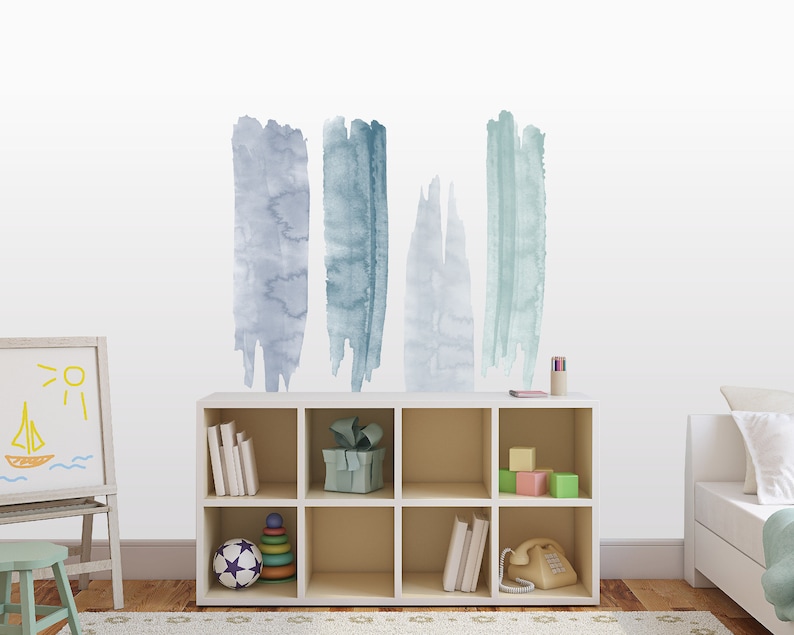 May include: A white bookshelf with six shelves, filled with books, toys, and a phone. The wall behind the bookshelf has five blue and gray watercolor brushstroke decals.
