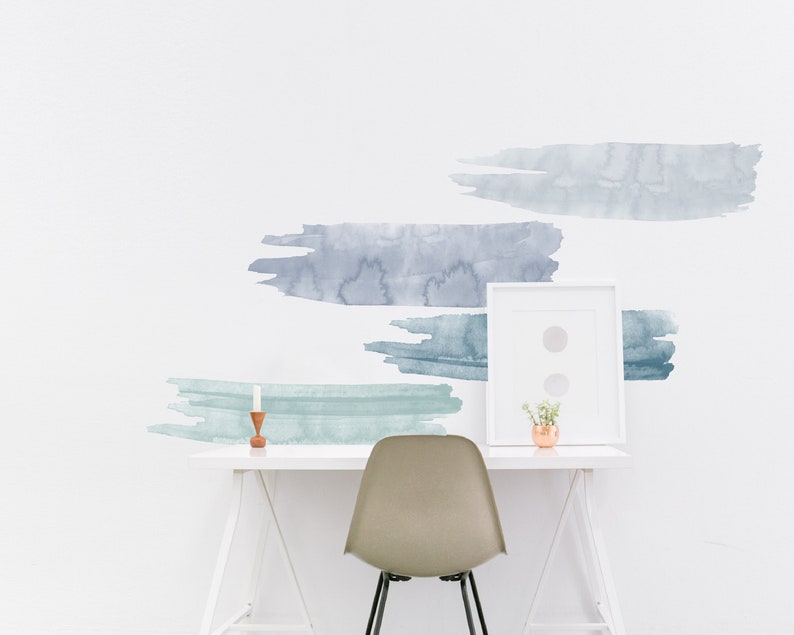May include: A white desk with a white chair and a white frame with a small plant in a copper pot. The wall behind the desk has blue and green watercolor brushstroke decals.
