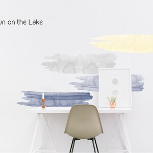 May include: A white desk with a white chair and a framed picture. The wall behind the desk has watercolor-style wall decals in shades of blue and yellow. The text "Sun on the Lake" is written in black at the top of the image.