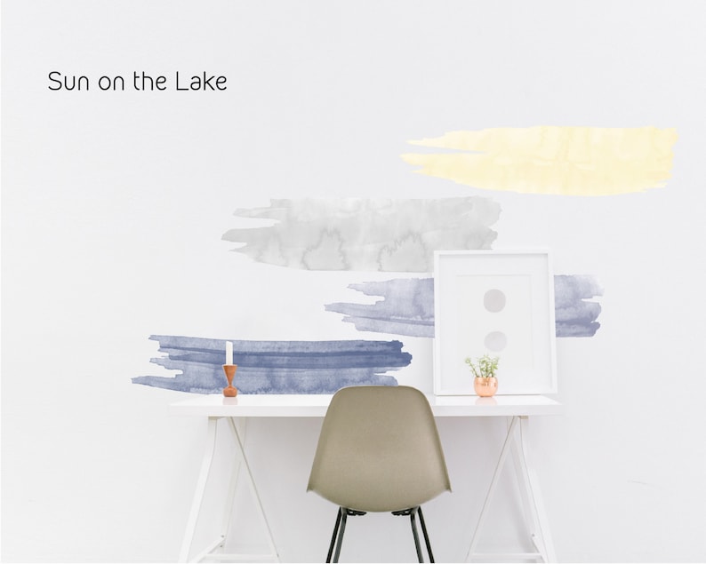 May include: A white desk with a white chair and a framed picture. The wall behind the desk has watercolor-style wall decals in shades of blue and yellow. The text "Sun on the Lake" is written in black at the top of the image.
