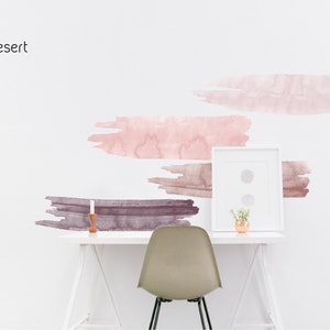May include: A white desk with a white chair and a framed picture. The wall behind the desk has a pink and brown watercolor design with the word "Desert" written in black at the top.