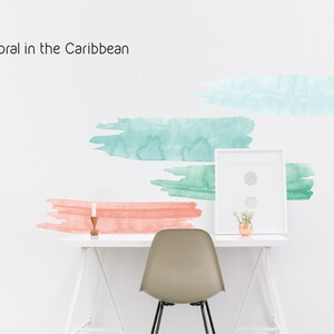 May include: A white desk with a white chair, a framed picture, a small plant, and a candle. The wall behind the desk has a watercolor design with the text "Coral in the Caribbean".