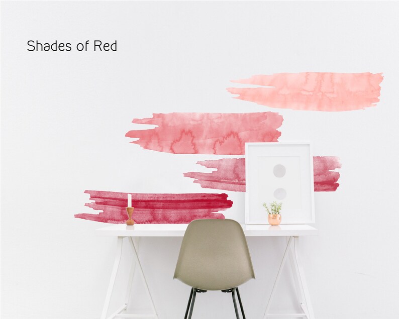 May include: Shades of Red wall decals featuring four abstract watercolor brushstrokes in various shades of red, pink, and burgundy. The decals are applied to a white wall above a white desk with a chair and a small potted plant.