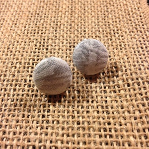 May include: Two silver and white fabric covered buttons with a subtle pattern. The buttons are on a brown hessian background.