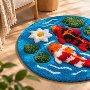 May include: A circular tufted rug featuring a blue water background with two koi fish in red, orange, white, and black. The design includes green lily pads and a single white flower with a yellow centre, accented by white wavy lines.