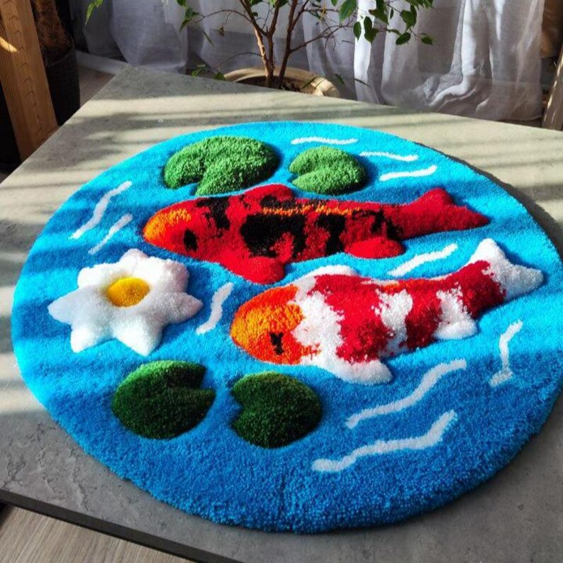 May include: A circular tufted rug featuring a vibrant blue water background with white ripple accents. The design includes two koi fish, one primarily red and black and the other red and white, surrounded by green lily pads and a white water lily.