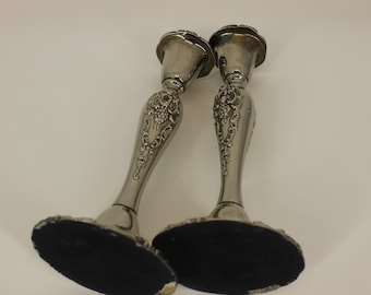 May include: A pair of silver candle holders with an ornate design. The candle holders have a floral pattern and a black felt base.