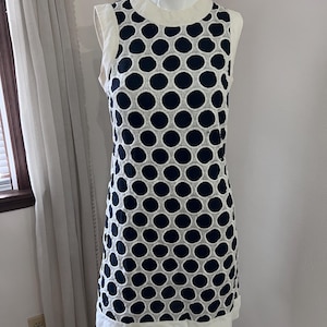 Puede incluir: Vestido sin mangas con estampado de lunares azul marino sobre fondo blanco. El vestido tiene cuello y dobladillo blancos. El vestido se exhibe en un maniquí.