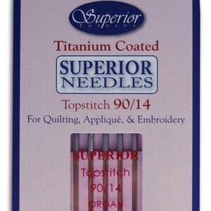 May include: A package of Superior Needles for quilting, appliqué, and embroidery. The package is white and purple with the text "Superior Needles" and "Topstitch 90/14". The needles are titanium coated.