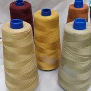 May include: A collection of spools of thread in various colors, including beige, yellow, brown, and burgundy. Each spool has a blue plastic core. The threads are tightly wound, creating a conical shape. Ideal for sewing, quilting, or other textile crafts.