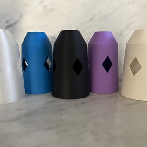 May include: Five cone-shaped objects in white, blue, black, purple, and cream. Each has a diamond-shaped cutout. The objects are arranged in a row on a light-colored surface. The objects appear to be made of plastic.