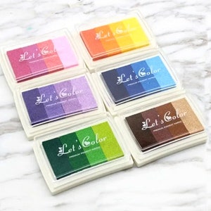 May include: Six multi-colored ink pads with the text "Let's Color" on each pad. The ink pads are arranged in two rows of three. Each ink pad has a different color combination of ink.