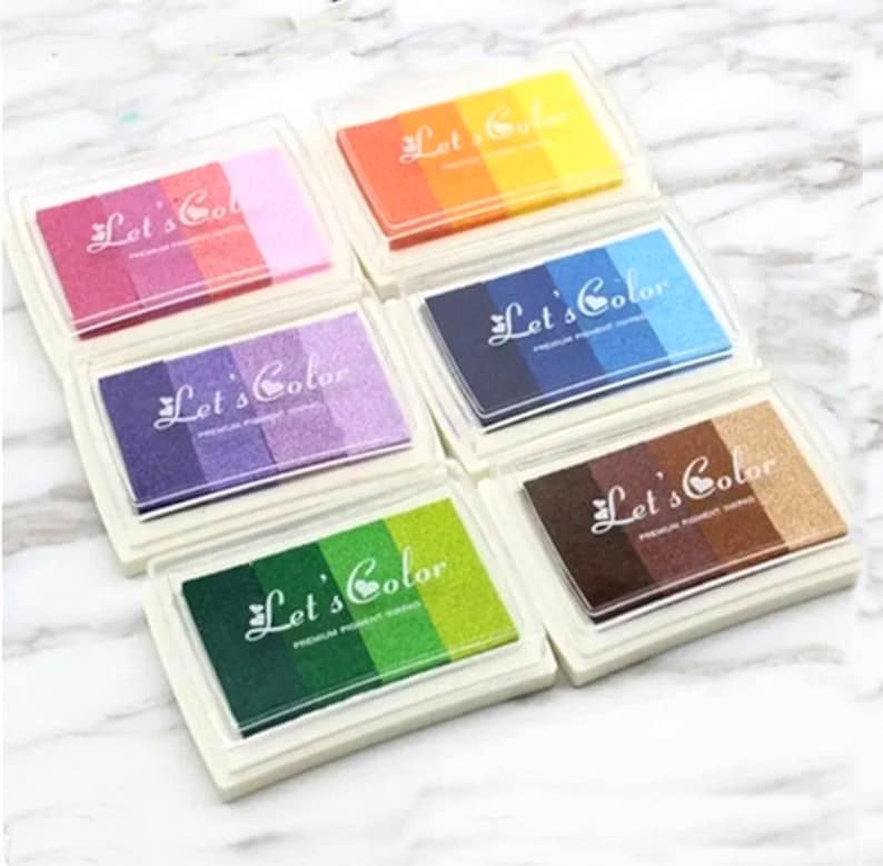 May include: Six multi-colored ink pads with the text "Let's Color" on each pad. The ink pads are arranged in two rows of three. Each ink pad has a different color combination of ink.