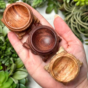 Puede incluir: Tres soportes de orbe de madera, cada uno con un patrón de veta de madera diferente. Los soportes están hechos de madera marrón oscuro, marrón rojizo y marrón claro. Los soportes están diseñados para sostener orbes de cristal u otros objetos pequeños.