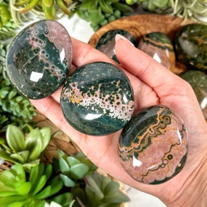 May include: Four green, pink, and brown ocean jasper palm stones. The stones are smooth and polished, with a variety of patterns and colors.