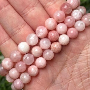 Könnte beinhalten: Eine Kette aus rosafarbenen und weißen Edelsteinperlen. Die Perlen sind rund und haben eine glatte, polierte Oberfläche.