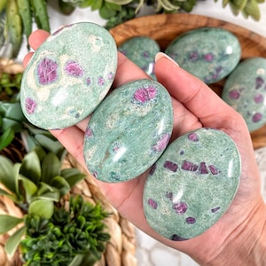 May include: A collection of green and pink ruby in zoisite tumbled stones. The stones are smooth and polished, with a variety of pink and green patterns.
