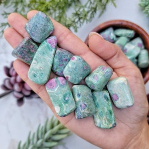 May include: A collection of green and pink ruby zoisite tumbled stones. The stones are smooth and polished, with a variety of shapes and sizes.