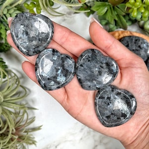 May include: Four gray and black heart-shaped labradorite crystal stones. The stones are smooth and polished.