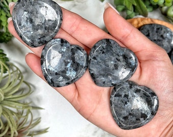 May include: Four gray and black heart-shaped labradorite crystal stones. The stones are smooth and polished.