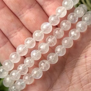 May include: Three strands of clear, round gemstone beads. The beads are a translucent white with subtle internal patterns. The beads are held in a hand, suggesting they are a bracelet or necklace.