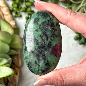 May include: A polished green and pink gemstone with a smooth, oval shape. The stone has a mottled pattern of green and pink.