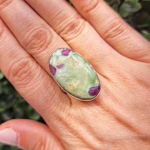 Peut inclure: Une bague en argent avec une pierre ovale verte et rose. La pierre précieuse présente un motif unique de tourbillons roses et verts.